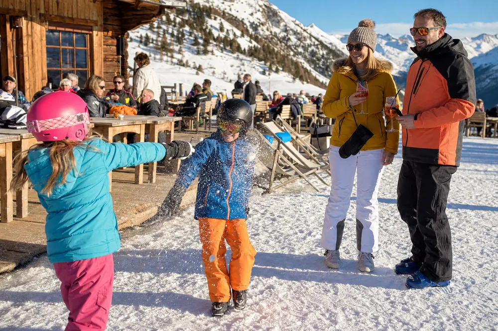 Barn med skihjelm leker i snøen utenfor en fjellrestaurant