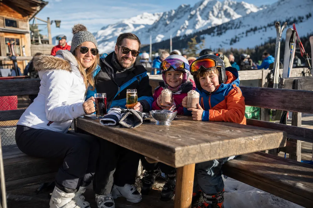 Familie med varm kakao på en solrik terrasse ved bakken